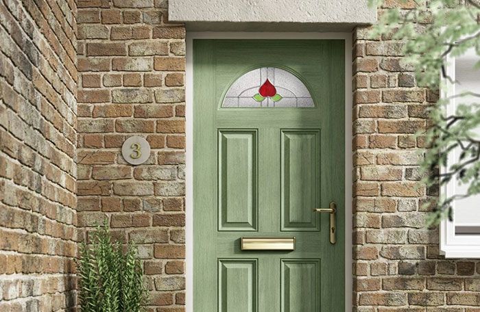 A sage green composite door with a decorative glass top on a stone house