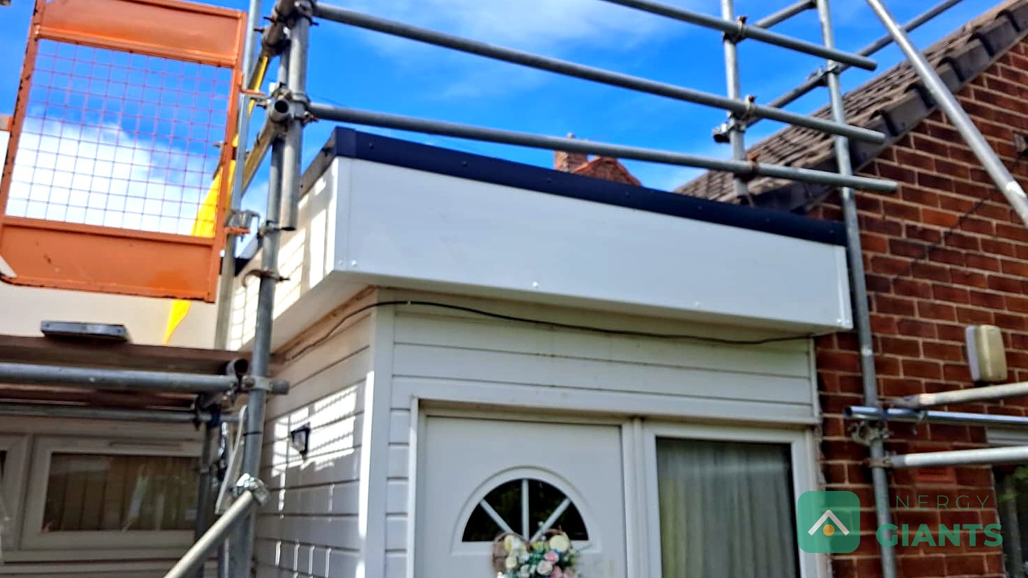 A finished black EPDM warm roof over a rear extension, seen from the scaffold beside the tiled main roof