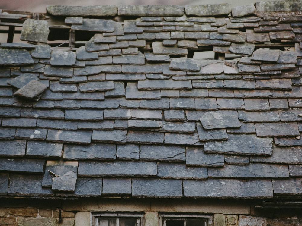 Old stone cottage roof with slipped, uneven and missing slates
