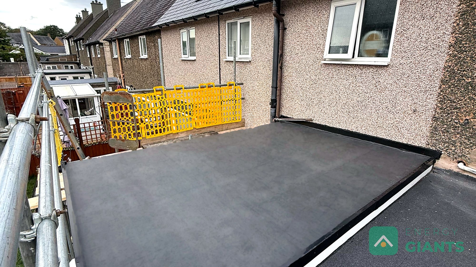 A finished black EPDM warm roof over a rear extension, seen from the scaffold with the back wall of the house behind