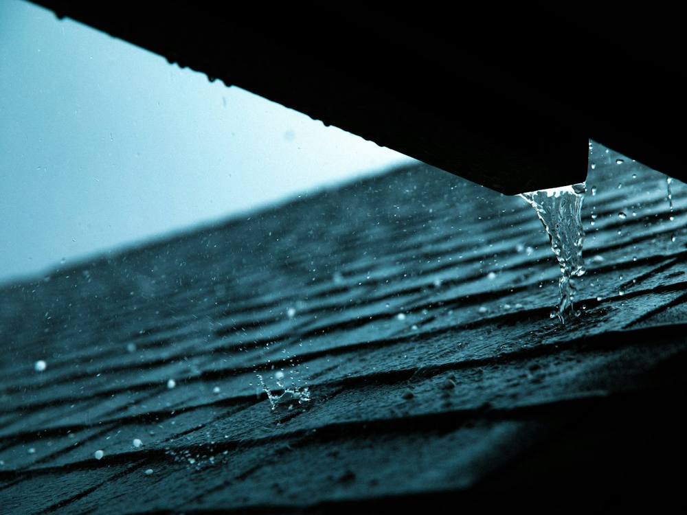 Rain running off a roof edge where a gutter should catch it