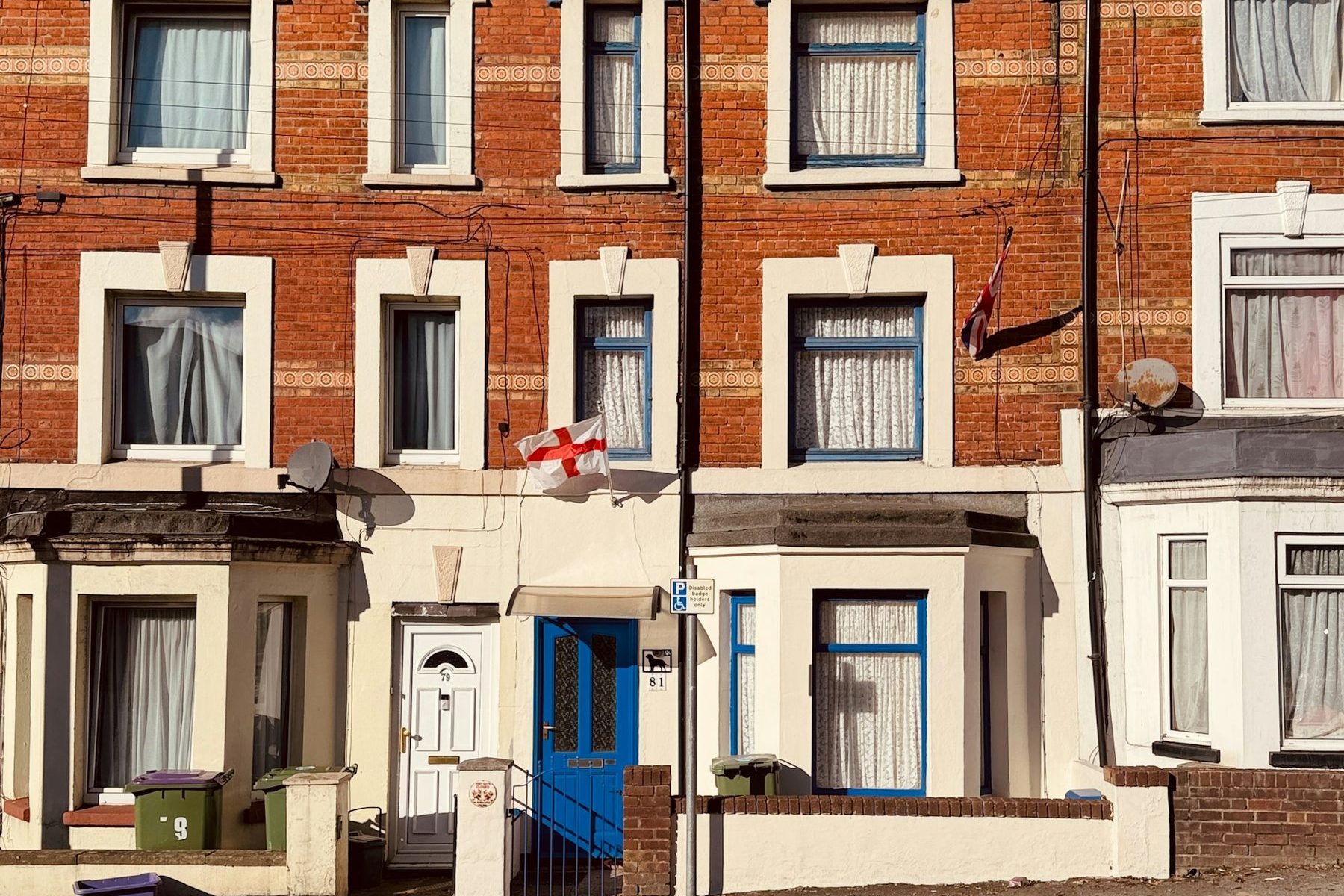 A row of red brick terraced houses with cream window surrounds, blue window frames and a blue front door